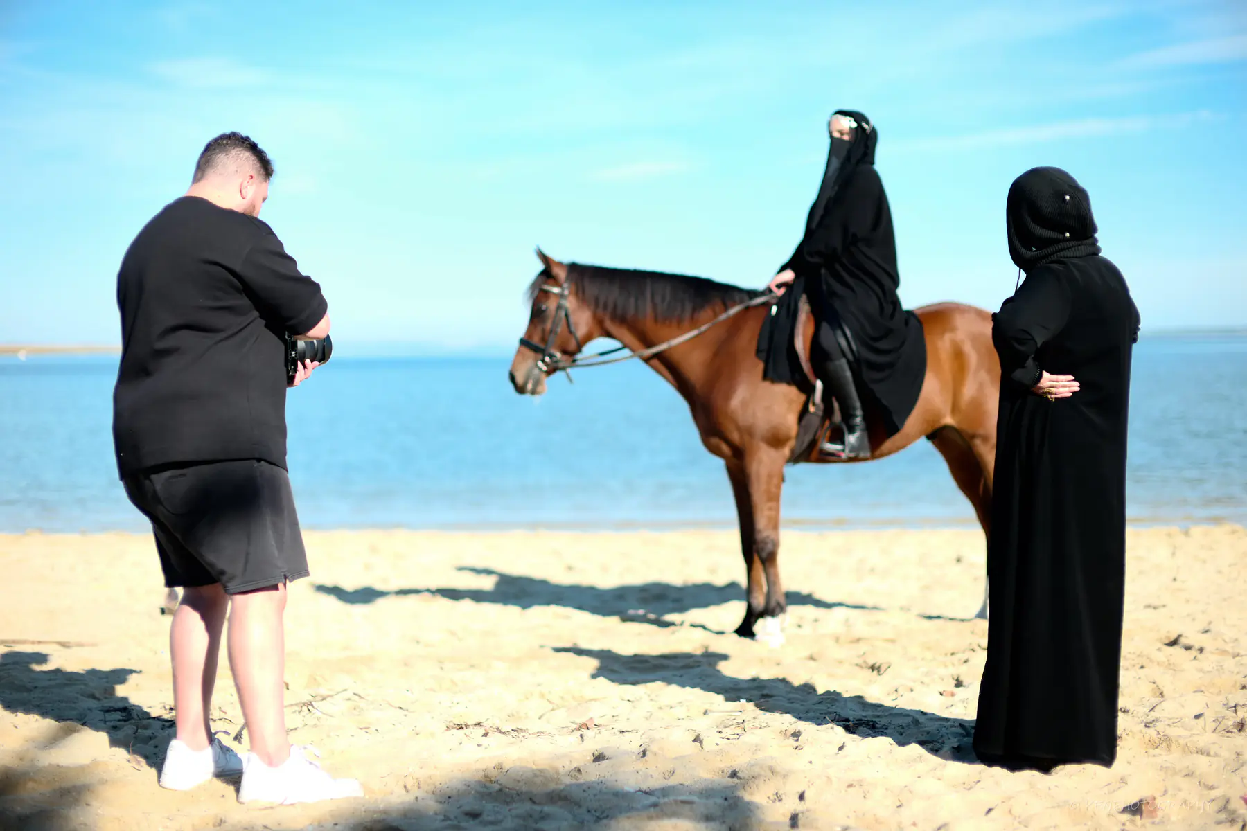 A photographer lines up a rider on a bay horse at the water’s edge