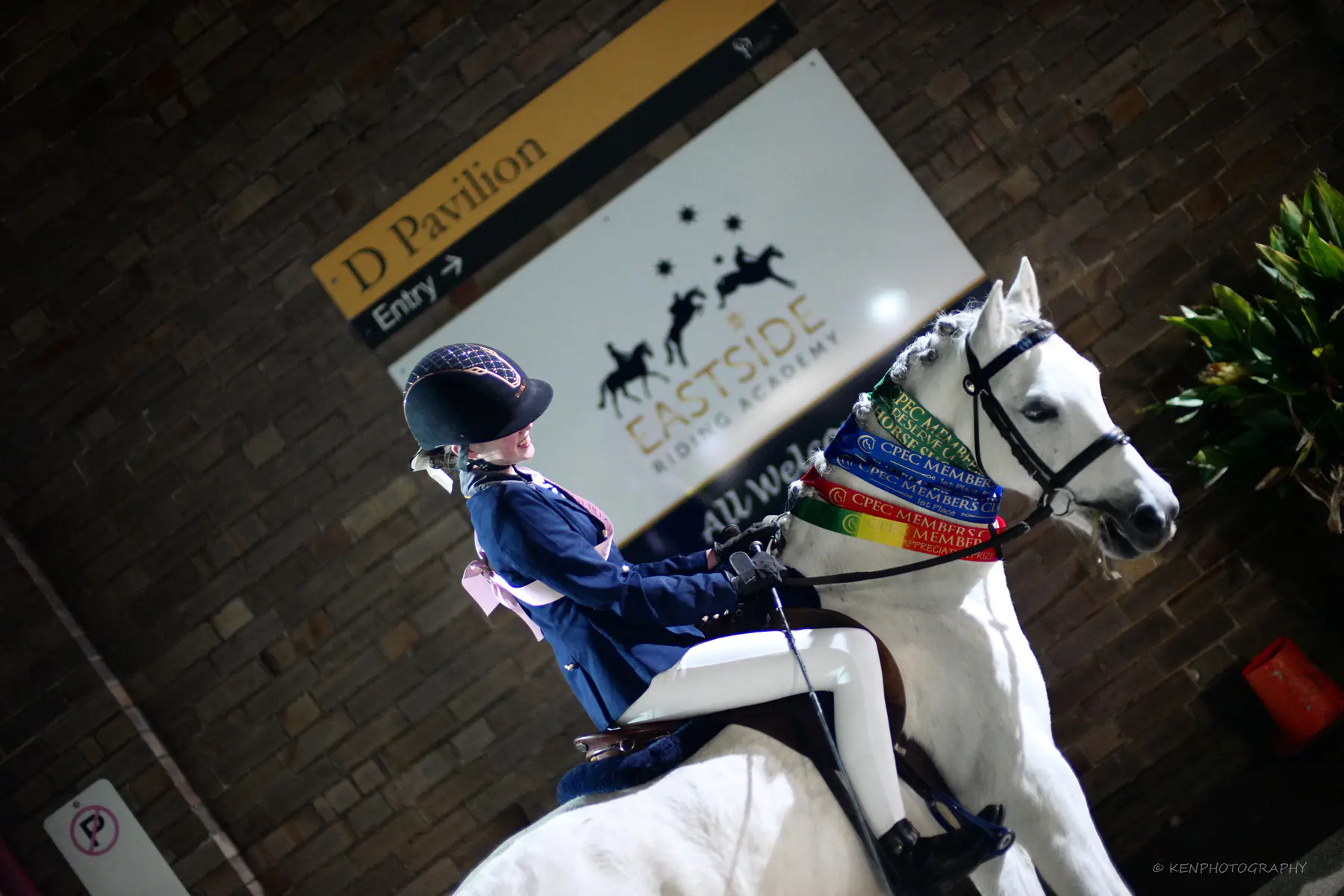 A young rider on a grey pony in front of the Eastside Riding Academy sign at dusk