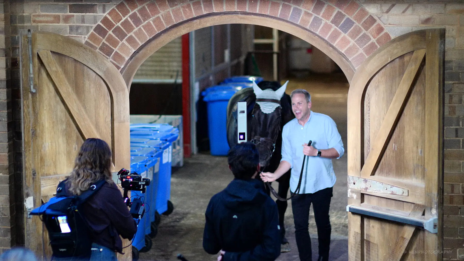 A camera operator and boom operator film a man at the brick stable archway